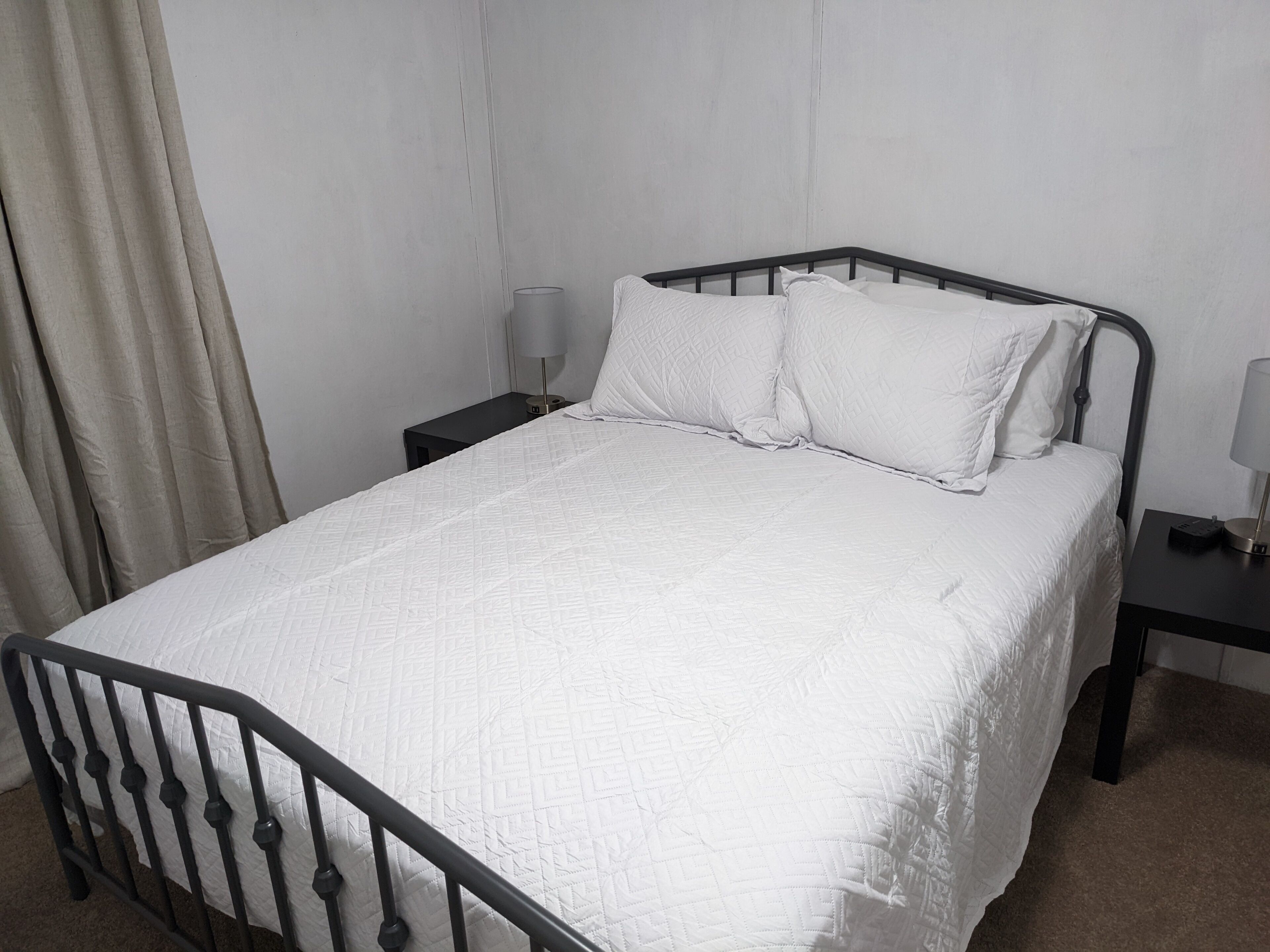 A single bed with a quilted white duvet, a black metal headboard, and two bedside tables with lamps.