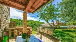 A rustic outdoor patio with stone walls, a wooden pergola, and a table with a tablecloth. - Beautiful home in Labin (Labin)