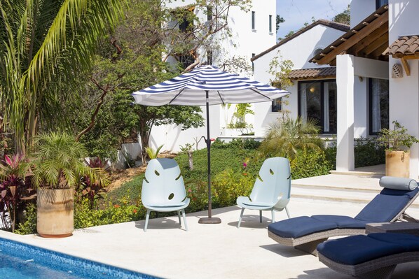 A poolside area with two lounge chairs, a striped umbrella, and a potted plant.