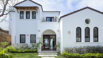 A two-story house with a white exterior, a balcony, and a front entrance with a glass door.