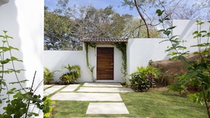 A garden pathway leading to a wooden door, surrounded by white walls and greenery. - Private, ocean view, gourmet kitchen (Sayulita)