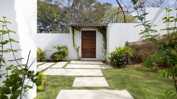 A garden pathway leading to a wooden door, surrounded by white walls and greenery.