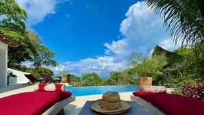 A poolside area with wicker lounge chairs and a table, a hat, and a view of the sky and trees. - Private, ocean view, gourmet kitchen (Sayulita)