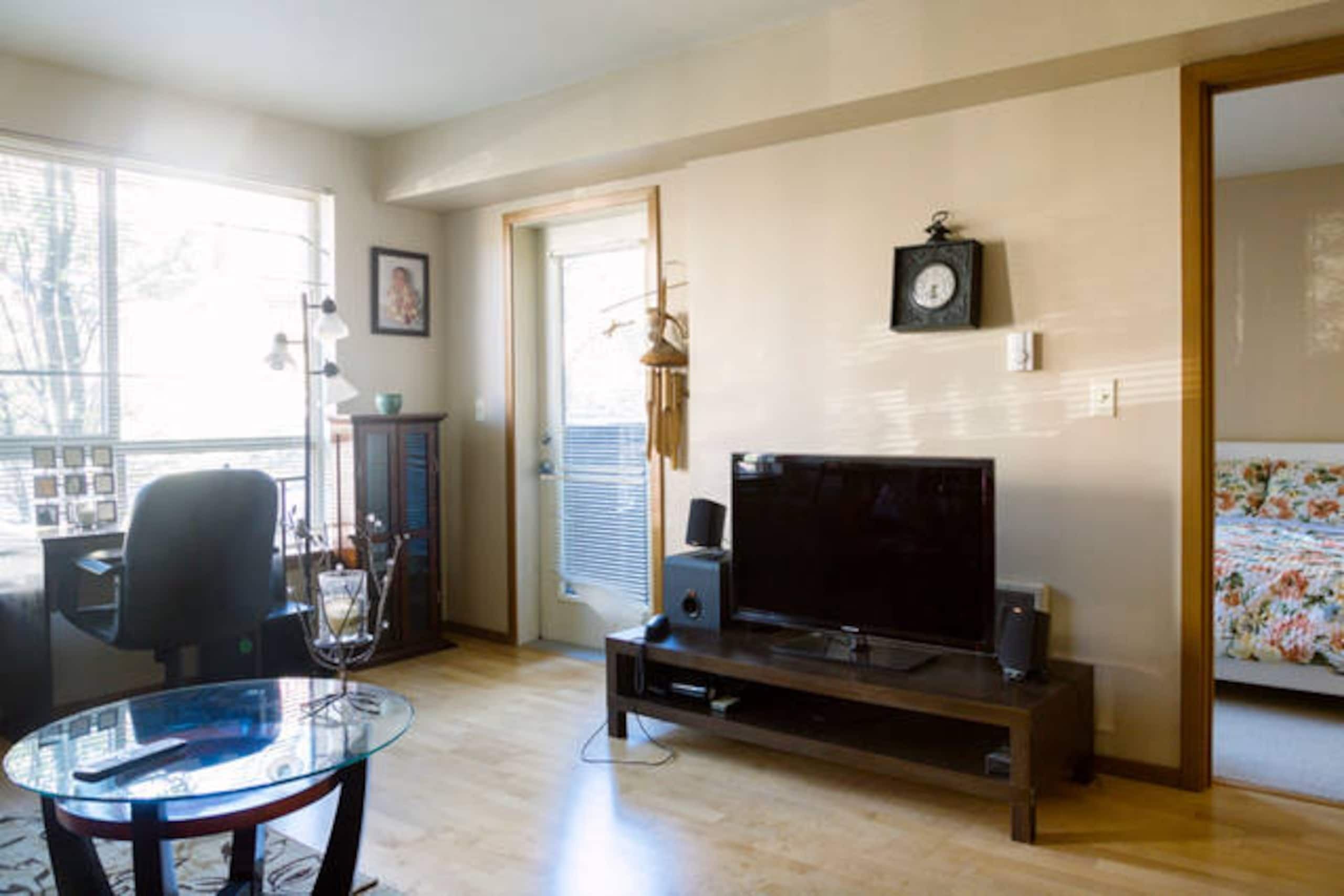 A living room with a television, a glass coffee table, a chair, and a door leading to another room.