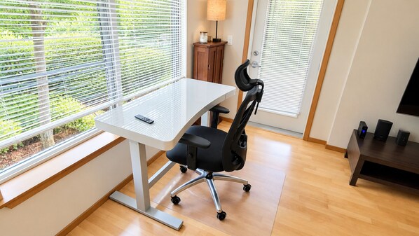 A modern office space with a white desk, black office chair, and a TV on a stand.
