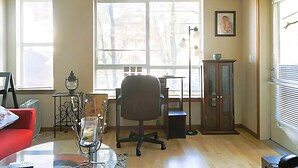Een kamer met een bureau, bureaustoel en een kast. Twee ramen zorgen voor natuurlijk licht.
