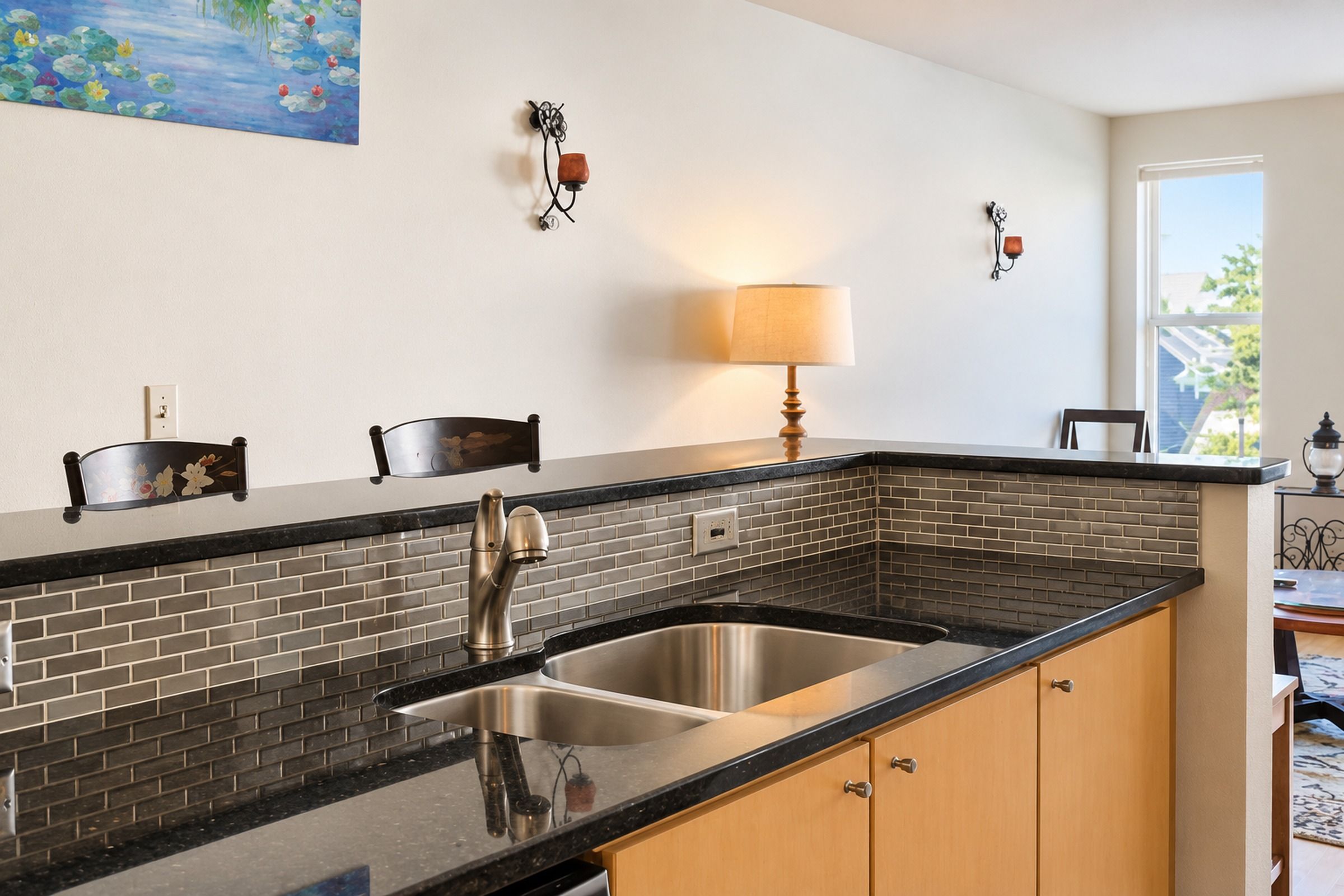 A kitchen with a stainless steel sink, black countertop, and wooden cabinets.