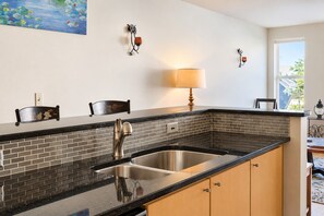 Una cocina con un lavamanos de acero inoxidable, encimera negra y armarios de madera.