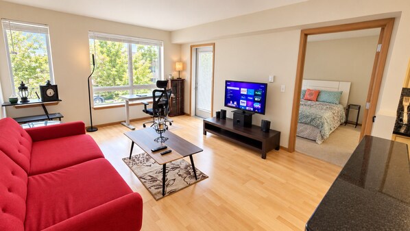 Una sala de estar moderna con un sofá rojo, una mesa de centro, un televisor y un comedor con una mesa y sillas negras.