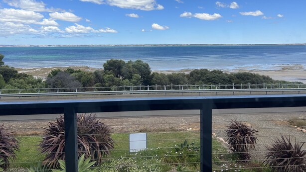 Vista costera con cielo despejado, una playa y una carretera al frente.
