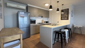 Una cocina moderna con una isla central, un refrigerador, un microondas y un lavamanos. Hay tres taburetes de bar y una trona.