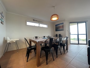 A dining area with a wooden table, black chairs, a high chair, a ceiling light, a window, and a door leading outside. - The Sandcastle, KI - Esplanade location (Kingscote)