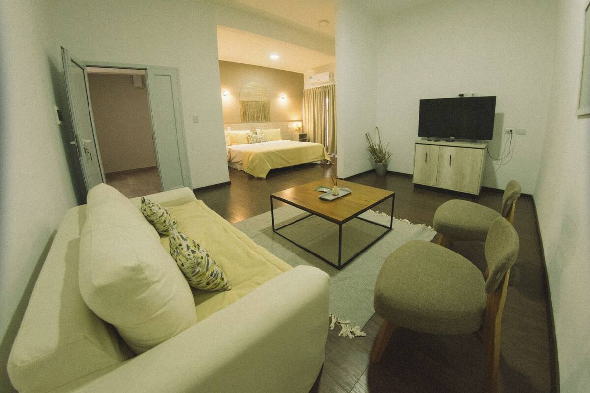 A hotel room with a living area, a bed, a television, and a small table.