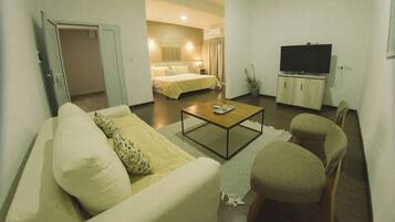 A hotel room with a living area, a bed, a television, and a small table.
