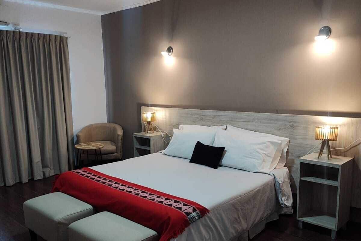 A modern hotel room with a large bed, two bedside tables, a chair, and a red throw blanket.