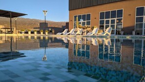 A swimming pool with lounge chairs, a lamp post, and a building with large windows and plants. - ENTRE VIÑEDOS RESORT HOTEL  (Schaqui)