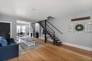 A modern living room with a staircase, a sofa, a coffee table, and a sign reading 'THE GATHERING PLACE'. - Heart of Plaza Midwood (Charlotte)