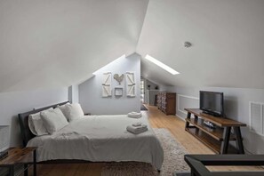 Ein Schlafzimmer mit einem Bett, einem Fernseher, einer hölzernen Kommode und einer weißen Wand mit gerahmten Bildern.