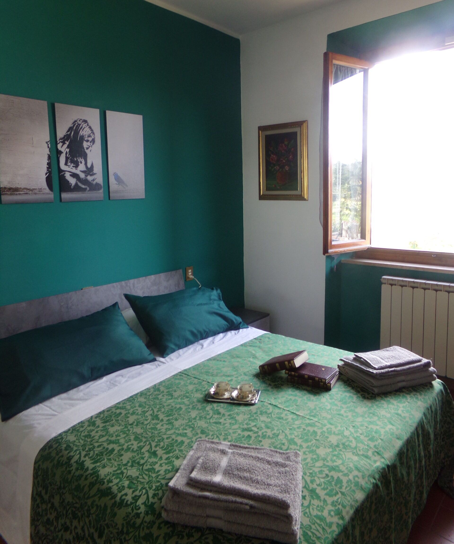 Un dormitorio con cama, almohadas, una ventana y obras de arte en la pared.