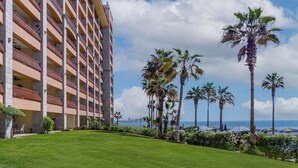 Un hotel con numerosi balconi, un prato curato e palme.