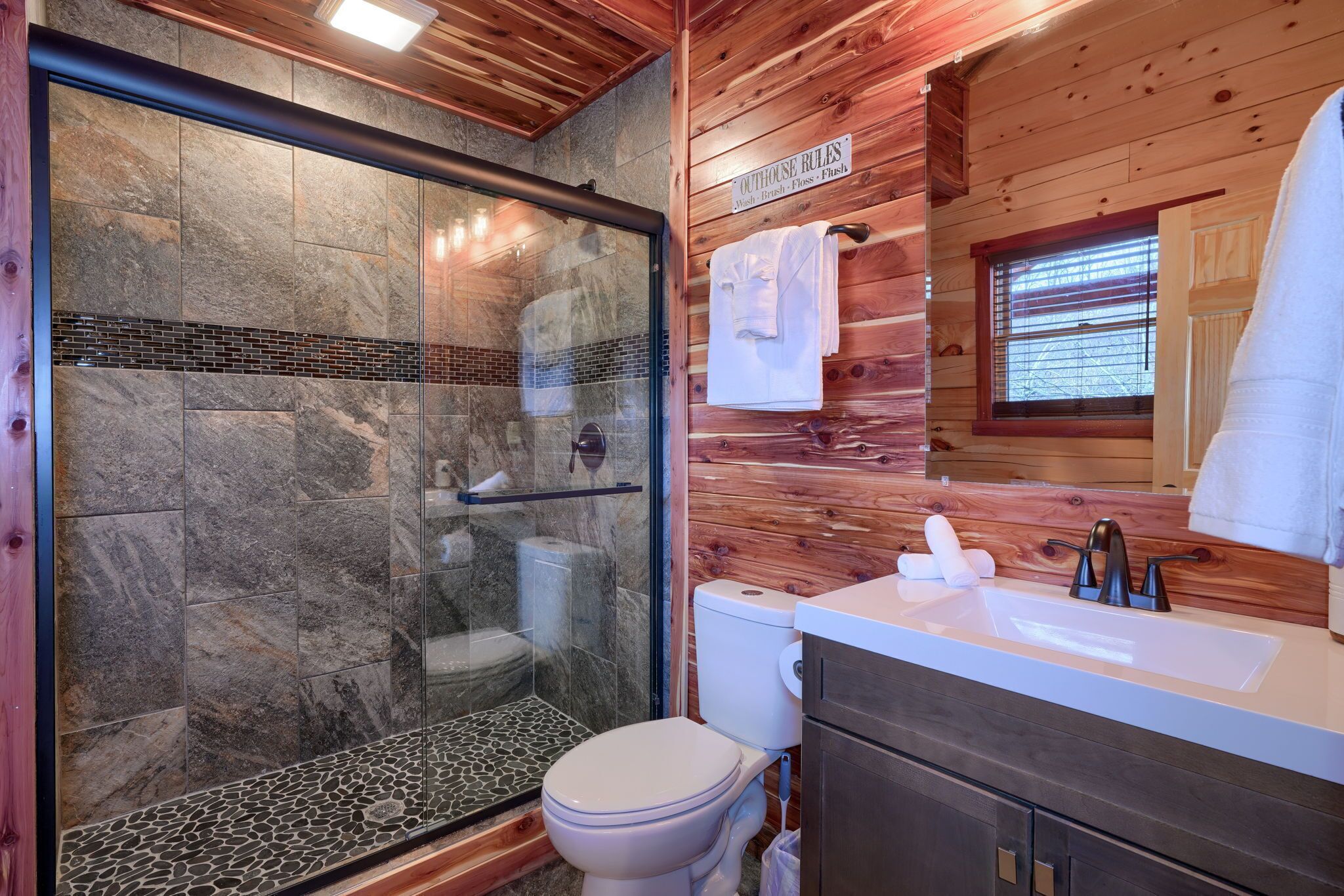 Un baño con ducha vidriada, inodoro y lavamanos con tocador de madera.