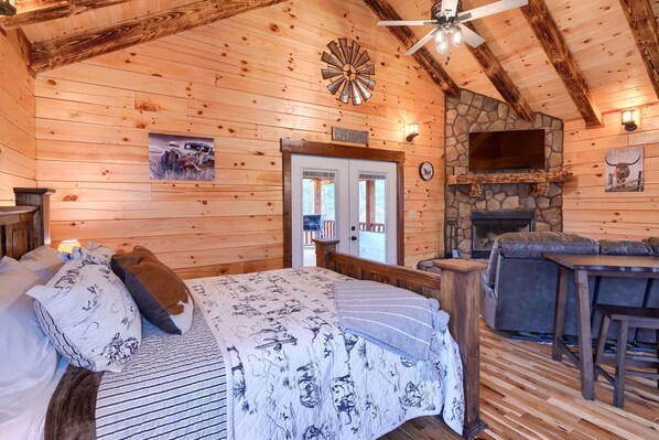 A cozy log cabin room with a bed, a stone fireplace, a television, and a wooden ceiling. - Cowboy Trail - Lovely Cabin for 2 in Hocking Hills (Logan)