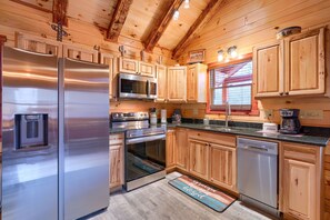 A modern kitchen with stainless steel appliances, wooden cabinets, and a large window. - Cowboy Trail - Lovely Cabin for 2 in Hocking Hills (Logan)