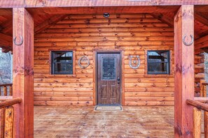 A wooden cabin with a central door, two windows with metal bars, and a welcome mat. - Cowboy Trail - Lovely Cabin for 2 in Hocking Hills (Logan)