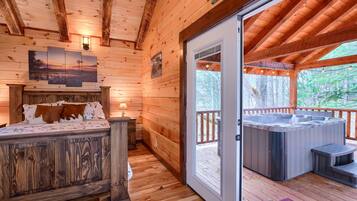 A wooden cabin interior with a bed, a hot tub, and a view of the outdoors.