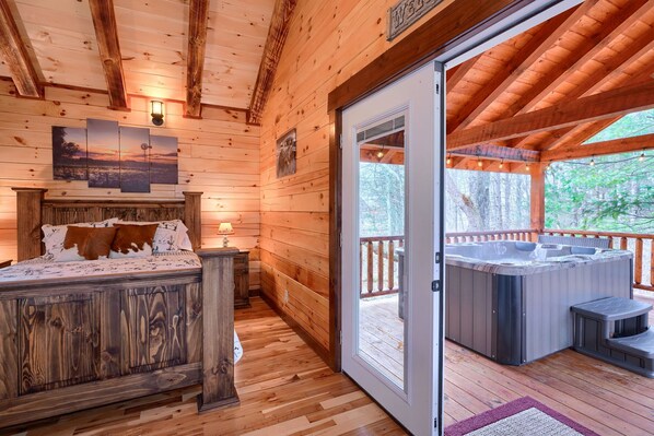 A wooden cabin interior with a bed, a hot tub, and a deck.