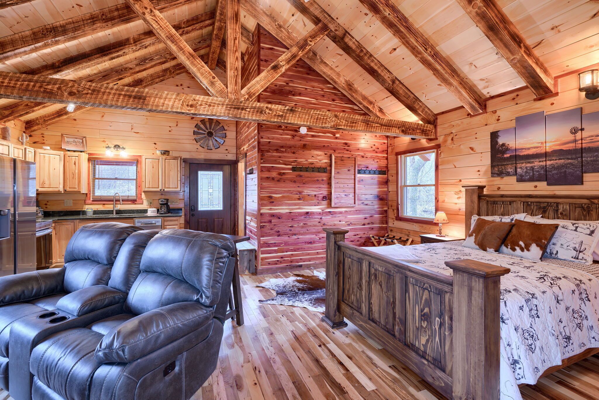 Ein rustikales Ferienhaus-Interieur mit einem großen Bett, Ledersessel, Holzböden und einer Küchenzeile.