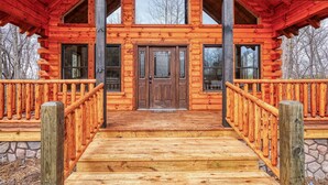 A log cabin with a wooden porch, a stone foundation, and a metal railing. - Bluebonnet Luxury Cabin - in the Hocking Hills (Logan)