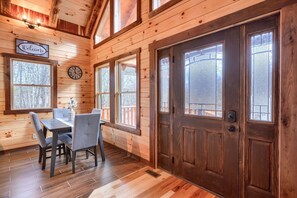 A wooden interior with a dining table, chairs, a clock, and a 'Welcome' sign.