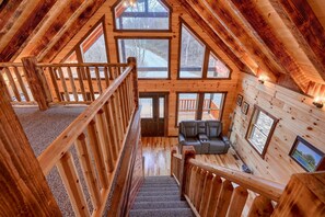 A log cabin interior with a wooden staircase, a sofa, and multiple windows offering views of the outdoors.