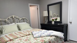 A neatly made bed with floral bedding, a dresser with a mirror, and a door to the right. - Loft apartment on Clifton, TN  Main Street Convenient, Cozy and Clean <br> (Clifton)