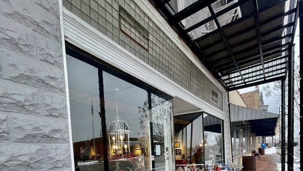 A storefront with large windows displaying various items, a covered outdoor seating area with tables and chairs, and a brick-paved walkway. - Loft apartment on Clifton, TN  Main Street Convenient, Cozy and Clean <br> (Clifton)