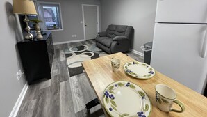 A compact kitchen with a refrigerator, a dining table with plates and a mug, a gray sofa, and a lamp. - Loft apartment on Clifton, TN  Main Street Convenient, Cozy and Clean <br> (Clifton)