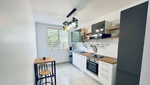Une cuisine moderne avec des armoires blanches, un plan de travail en bois et un four encastré. On y trouve un petit coin repas avec une table et deux chaises.