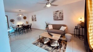 Un salon moderne comprenant un coin repas, un ventilateur de plafond et des œuvres d’art accrochées aux murs.