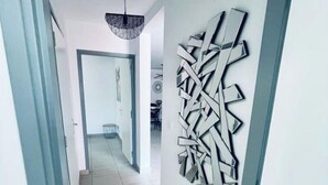 Un couloir agrémenté d’une œuvre d’art murale abstraite et moderne, d’un luminaire au plafond et d’un sol carrelé.