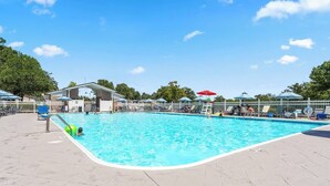 A swimming pool with a white fence, lounge chairs, and umbrellas.