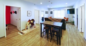 A room with a wooden floor, a dining table with two chairs, a sofa, and a TV mounted on the wall.