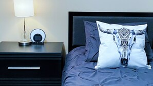 Ein ordentlich bezogenes Bett mit einem gemusterten Kissen, einer Nachttischlampe und einem kleinen Tisch mit Lampe und Uhr.