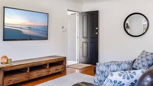 A living room with a large TV, a wooden entertainment unit, a black door, and a patterned sofa. - "Eastside Haven" - Central & Convenient! (East Toowoomba)