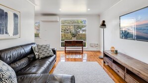 A modern living room with a leather sofa, a wooden coffee table, and a large window offering a view of the outdoors. - "Eastside Haven" - Central & Convenient! (East Toowoomba)