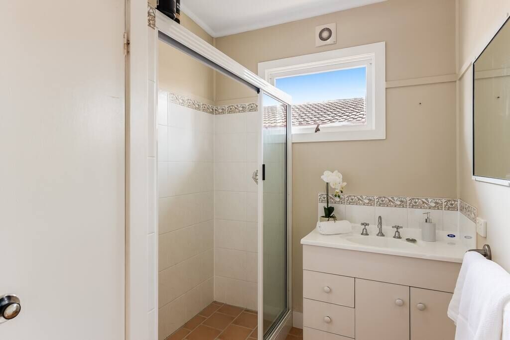 A bathroom with a glass shower enclosure, a white sink with a mirror above it, and a tiled backsplash.