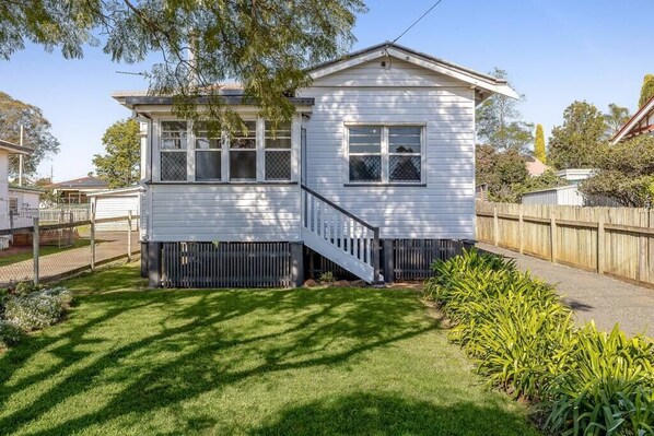 A two-story house with a front porch, a small deck, and a fenced backyard. - Cheerful, Cosy Cottage - Near Rose Garden! (Newtown)