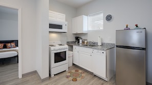 A compact kitchen with white cabinetry, a stainless steel refrigerator, a microwave, and a stove. - New! Hippy Haven Suite in East! 4bd! (Nashville)
