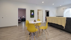 A modern living room with a dining area, featuring a round table and yellow chairs, a grey sofa, and a decorative wall hanging. - New! Hippy Haven Suite in East! 4bd! (Nashville)