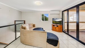 Ein modernes Wohnzimmer mit einer gebogenen Couch, einer Holzkommode und einem großen Fenster mit Blick auf Grünflächen.